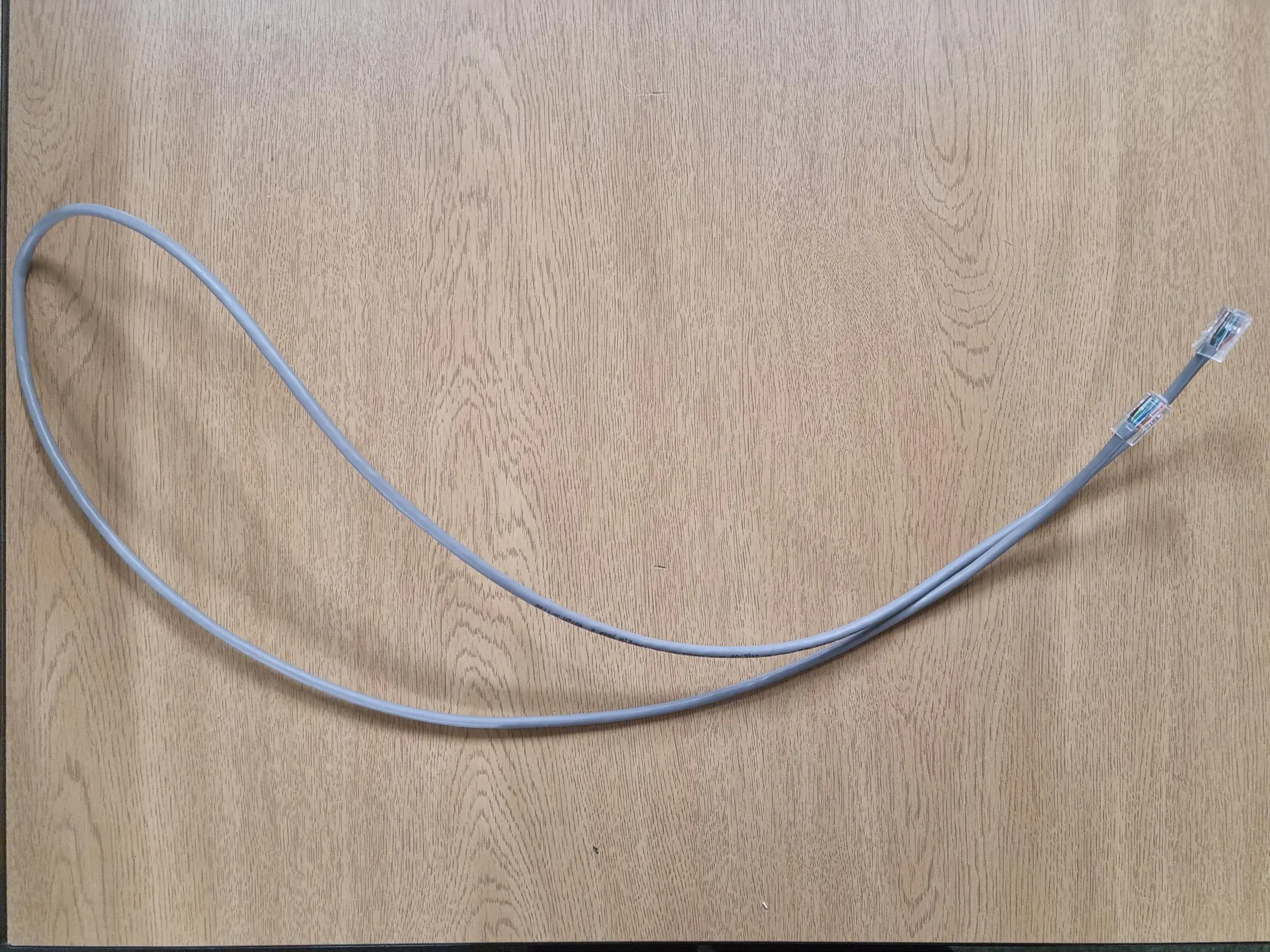 A coiled gray Ethernet cable with clear plastic connectors on both ends, lying on a wood grain desktop.